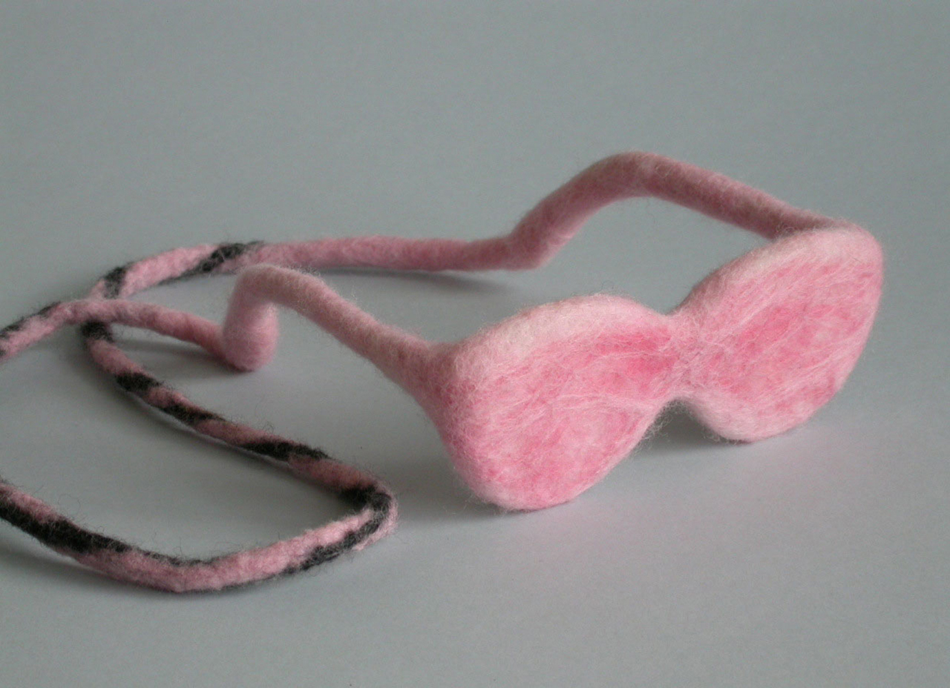 foto van een met roze wol in gevilte bril met een koord dat doorloopt vanuit de poten.